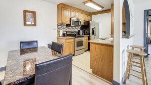 A modern kitchen with wooden cabinets, a granite countertop, stainless steel appliances, and a dining area with a marble table and leather chairs. - WFH-Friendly Las Vegas Condo: 2 Mi to Strip! (Las Vegas)