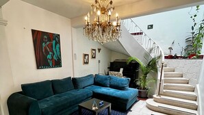 Una sala de estar con un sofá modular, una mesa de centro, una araña, una escalera y un cuadro en la pared.