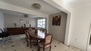 Un comedor con una mesa redonda, seis sillas, un aparador de madera y una araña.