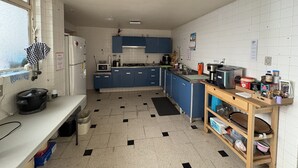 Una cocina con paredes de azulejos blancos, armarios azules, un mantel a cuadros negros y blancos y una repisa de madera con utensilios de cocina.