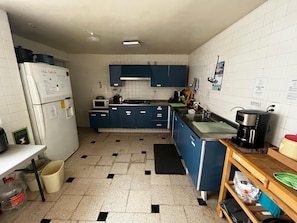 A kitchen with white tiled walls, blue cabinets, a refrigerator, microwave, stove, sink, and a coffee maker. - Habitación cerca de Mitikah (Mexico City)