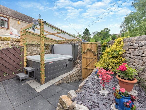 A hot tub with a wooden pergola, stone walls, and potted plants.