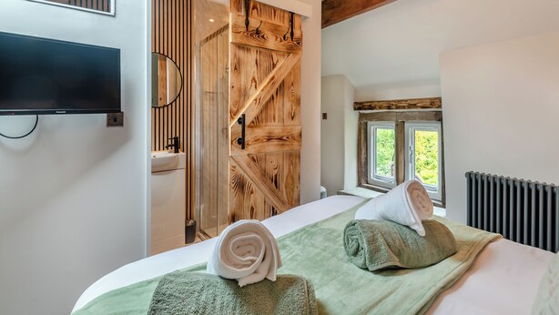 A hotel room with a bed, a television, a wooden door, and a window with a view of greenery. - 2 bedroom accommodation in Bonsal, near Matlock (Bonsal, near Matlock)