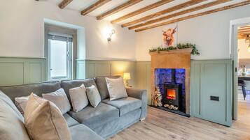 A cozy living room with a grey sofa, a fireplace, and exposed wooden beams.