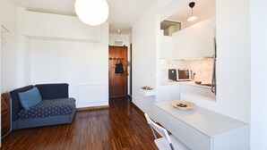 A modern, well-lit room with a wooden floor, a sofa with patterned cushions, a dining area with a white table and chairs, and a kitchenette with a microwave and toaster. - Stunning apartment in Bordighera (Bordighera)