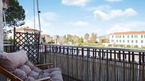 A balcony with a cushioned chair, a bamboo fence, and a view of buildings and trees. - Stunning apartment in Bordighera (Bordighera)