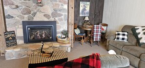 Ett mysigt vardagsrum med en öppen spis i sten, en soffa, ett soffbord och en liten matplats.