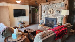 A cozy living room with a stone fireplace, a television, and comfortable seating. - Cozy Cottage with so many amenities, on beautiful Little Hills Lake in Wautoma (Wautoma)