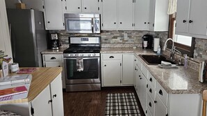 A kitchen with white cabinets, a stainless steel refrigerator, a microwave, a stove, and a sink. - Cozy Cottage with so many amenities, on beautiful Little Hills Lake in Wautoma (Wautoma)