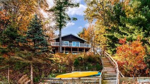 A cabin with a wooden deck and a kayak, surrounded by autumn foliage. - Cozy Cottage with so many amenities, on beautiful Little Hills Lake in Wautoma (Wautoma)