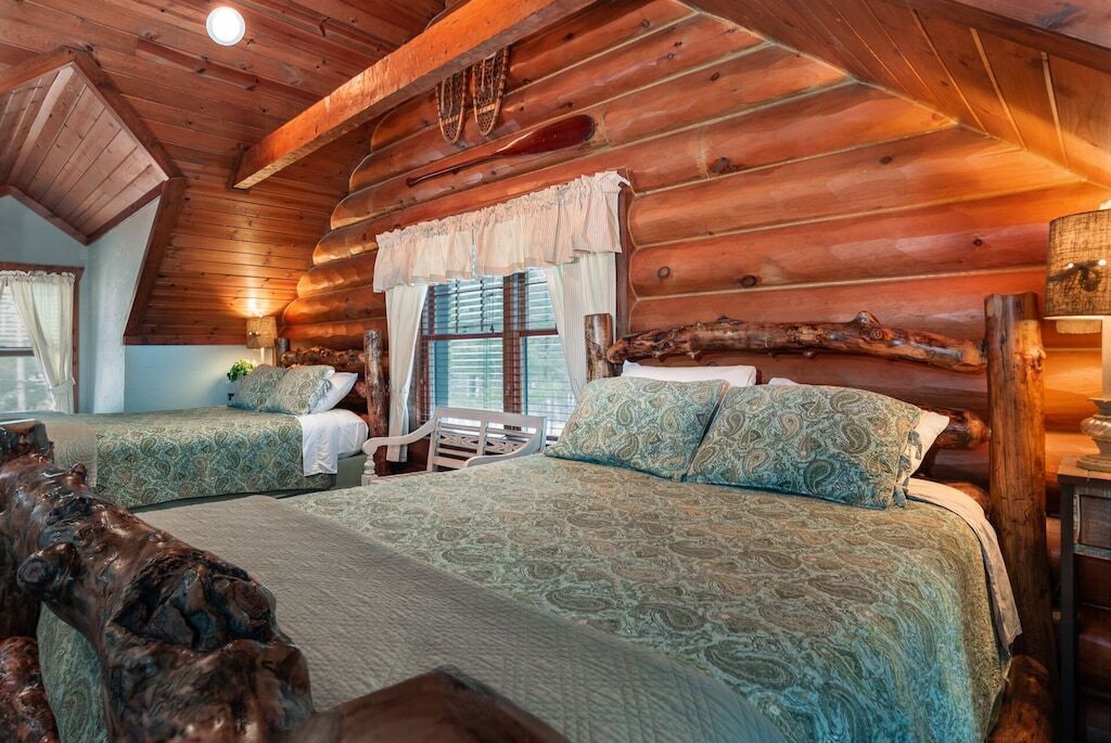 Quarto de cabana de tronco com duas camas, teto de madeira e decoração rústica.