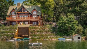Une cabane en rondins avec un balcon, un quai avec des bateaux et un petit abri au bord de l’eau.