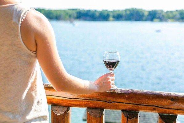 A person holding a wine glass, overlooking a body of water with a wooden railing.
