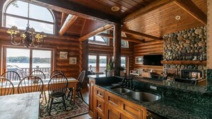 Une cuisine de style rustique, aménagée comme une cabane, avec un mur en pierre, des armoires en bois et une grande fenêtre donnant sur un lac.