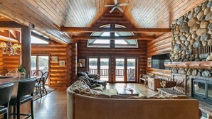 L’intérieur d’une cabane en rondins, avec une cheminée en pierre, un grand canapé et un coin repas.