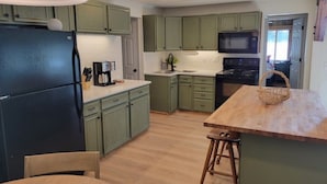A kitchen with green cabinets, a black refrigerator, a wooden table, and a microwave. - Amazing view, hot tub, sauna, fireplace, pet friendly, pier, kayaks, paddleboard (Wautoma)