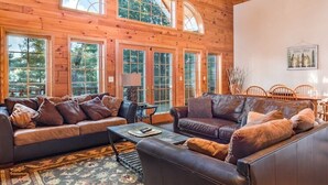 A spacious living room with leather sofas, a coffee table, and a large window overlooking a forest. - Free nite w/wknd offseason;logcabin lake hottub kayak paddleboard pier fireplace (Wild Rose)