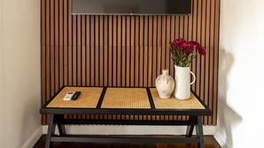 A room with a wooden slat wall, a flat-screen TV mounted above a bench, and a vase with flowers on the bench. - Furnished Bachelor in Hollywood (Los Angeles)