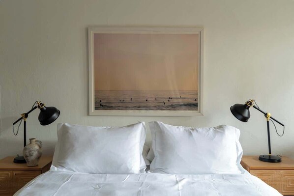 Une chambre d’hôtel avec un lit, deux lampes de chevet, un tableau encadré représentant une scène de plage et un vase posé sur la table de chevet.