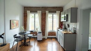 A compact kitchen with a brick wall, a dining area with a table and chairs, and a microwave above the counter. - Furnished Bachelor in Hollywood (Los Angeles)