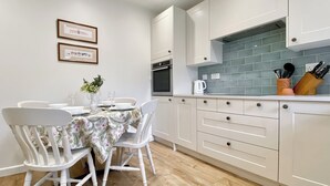Een moderne keuken met witte kasten, een betegelde spatwand en een eethoek met een tafelkleed met bloemenmotief.
