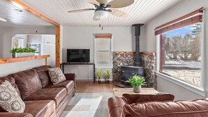 Ein gemütliches Wohnzimmer mit einer braunen Ledersofa, einem Kamin aus Naturstein, einem Fernseher und einem großen Fenster mit Blick ins Freie.