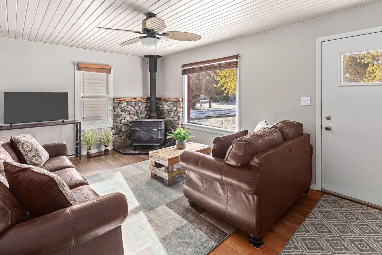 Ein Wohnzimmer mit Kamin aus Stein, Ledersofas, einem Fernseher und einem Deckenventilator.