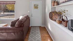 Ein Zimmer mit einem braunen Ledersofa, einem gemusterten Teppich, einer Tür mit einem gerahmten Bild und Regalen mit Körben und einer Vase.