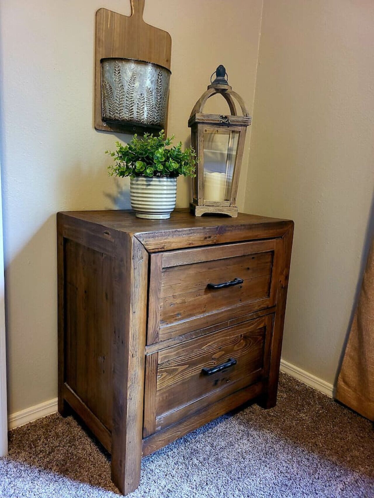 A wooden nightstand with three drawers and a potted plant on top.