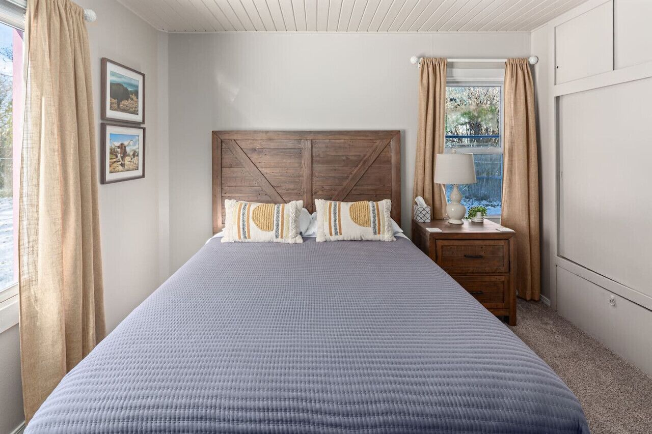 A bedroom with a large bed, wooden headboard, two bedside tables, a nightstand, and a window with curtains.