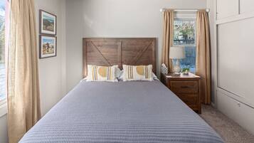 A bedroom with a large bed, wooden headboard, two bedside tables, a nightstand, and a window with curtains.