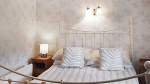 Een net opgemaakt bed met een sierkussen met bladmotief, een bedlamp en een wandlamp.