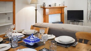 Een eettafel gedekt met borden, glazen en bestek, een bank, een televisie en een lamp in een kamer met een open haard.