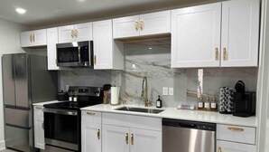 A modern kitchen with white cabinets, stainless steel appliances, and marble countertops.