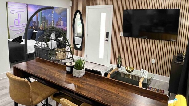 A modern living room with a wooden dining table, a sofa, a TV mounted on the wall, and a cityscape painting.