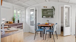 A dining area with a wooden table, blue chairs, and a green wall-mounted shelf with glassware. - 3 bedroom gorgeous home in Børkop (Børkop)