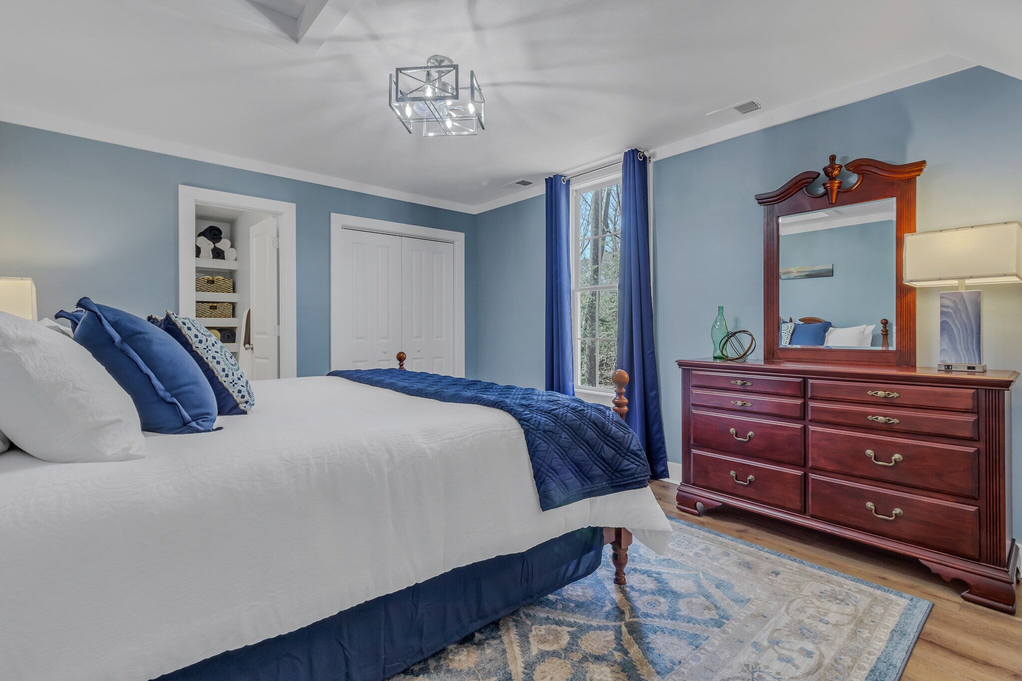 A bedroom with a large bed, a dresser, a mirror, and a door leading to a closet.