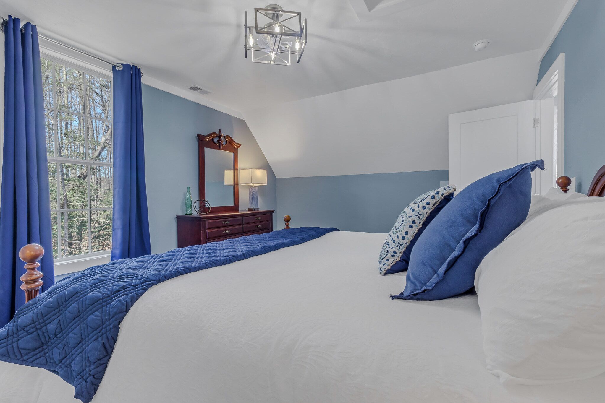 Un dormitorio con una cama grande, un tocador, un espejo y una ventana con cortinas.