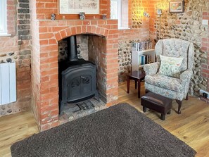 A cozy living room with a brick fireplace, a comfortable armchair, a bookshelf, and a rug. - 2 bedroom accommodation in Ridlington (Ridlington)
