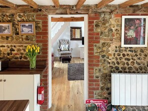 A rustic interior with exposed brick walls, a wooden ceiling, a fireplace, a dining area, and a hallway leading to another room. - 2 bedroom accommodation in Ridlington (Ridlington)