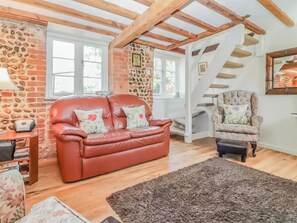 A cozy living room with a red leather sofa, a floral armchair, and a staircase leading to an upper level. - 2 bedroom accommodation in Ridlington (Ridlington)