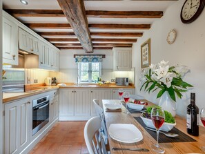 Cucina con mobili bianchi, soffitto in legno e zona pranzo con tavolo apparecchiato per due.