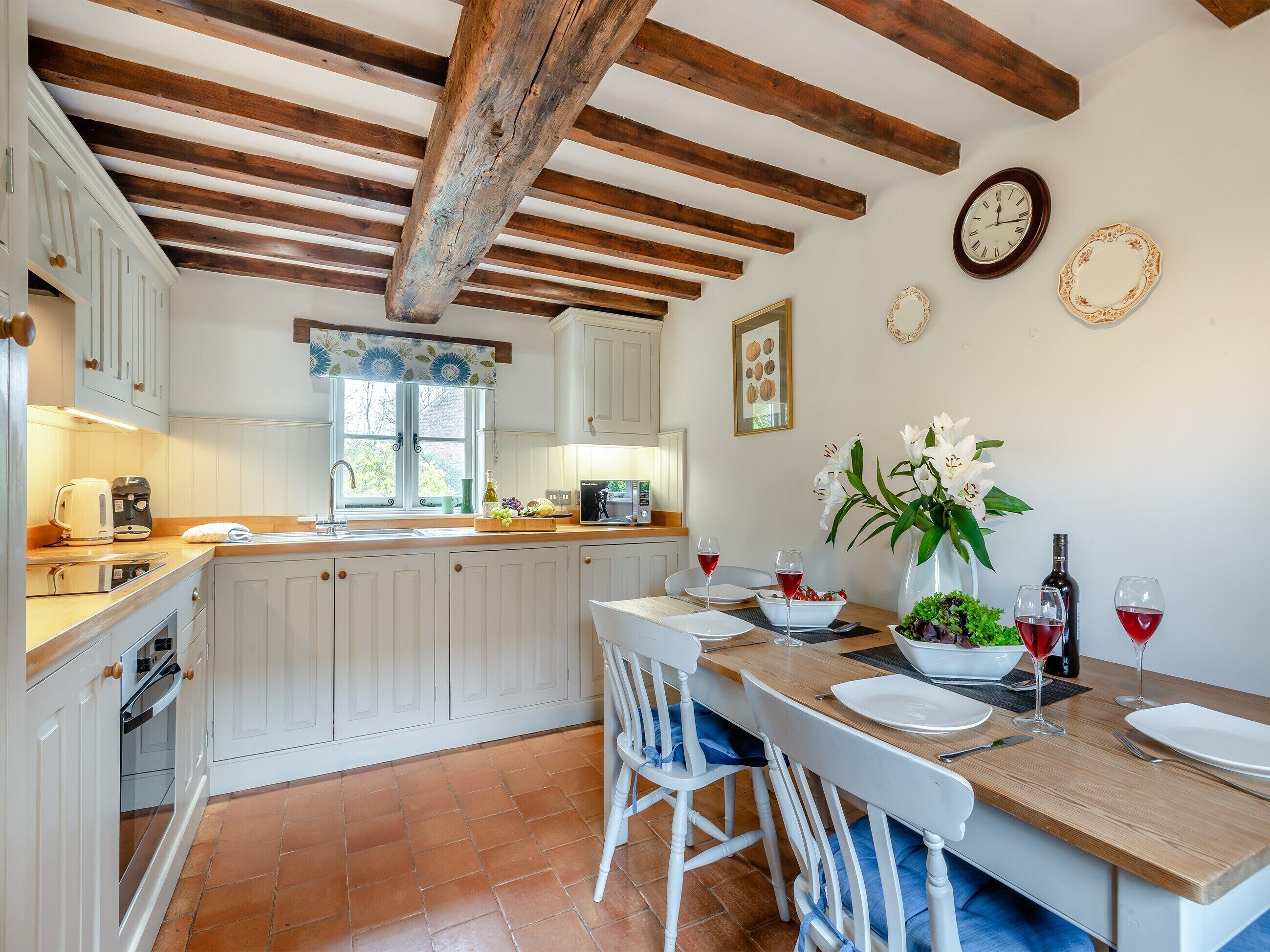 A kitchen with white cabinets, a wooden ceiling, and a dining area with a table set for two.