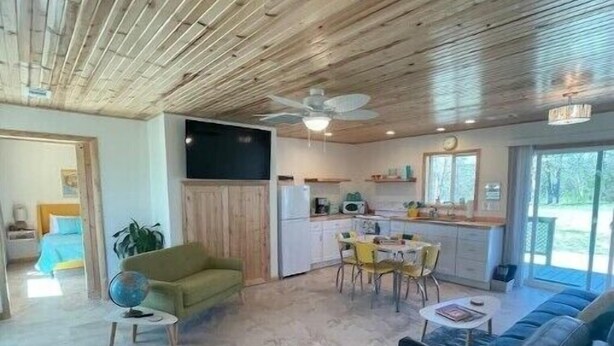 Uma sala ampla com teto de madeira, um sofá, uma mesa de jantar com cadeiras e uma área de cozinha com televisão de tela plana.