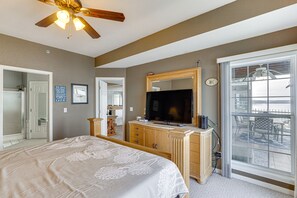 Un dormitorio con una cama grande, televisor, cómoda y puerta corrediza de vidrio que da a un balcón.