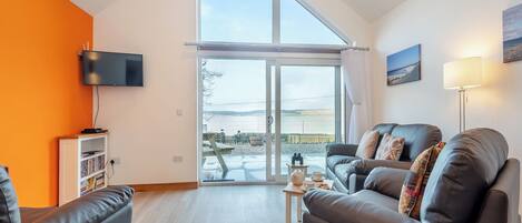 A modern living room with a large window, a flat-screen TV, a bookshelf, and a sofa.