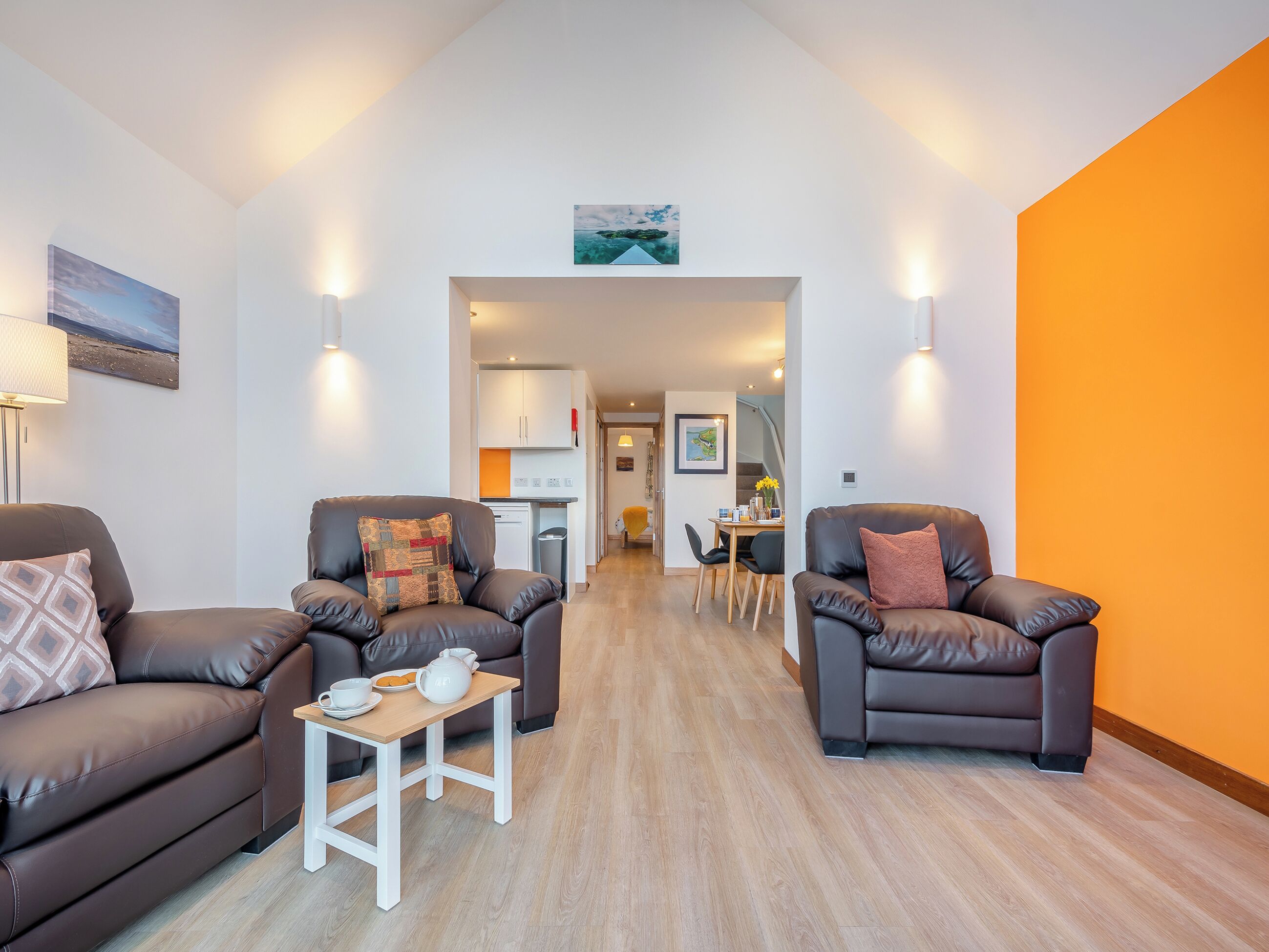 Una sala de estar moderna con dos sofás de cuero, una pequeña mesa de centro de madera y una cocina al fondo.