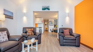 A modern living room with two leather sofas, a small wooden coffee table, and a kitchen in the background. - 2 bedroom accommodation in Lochranza (Lochranza)
