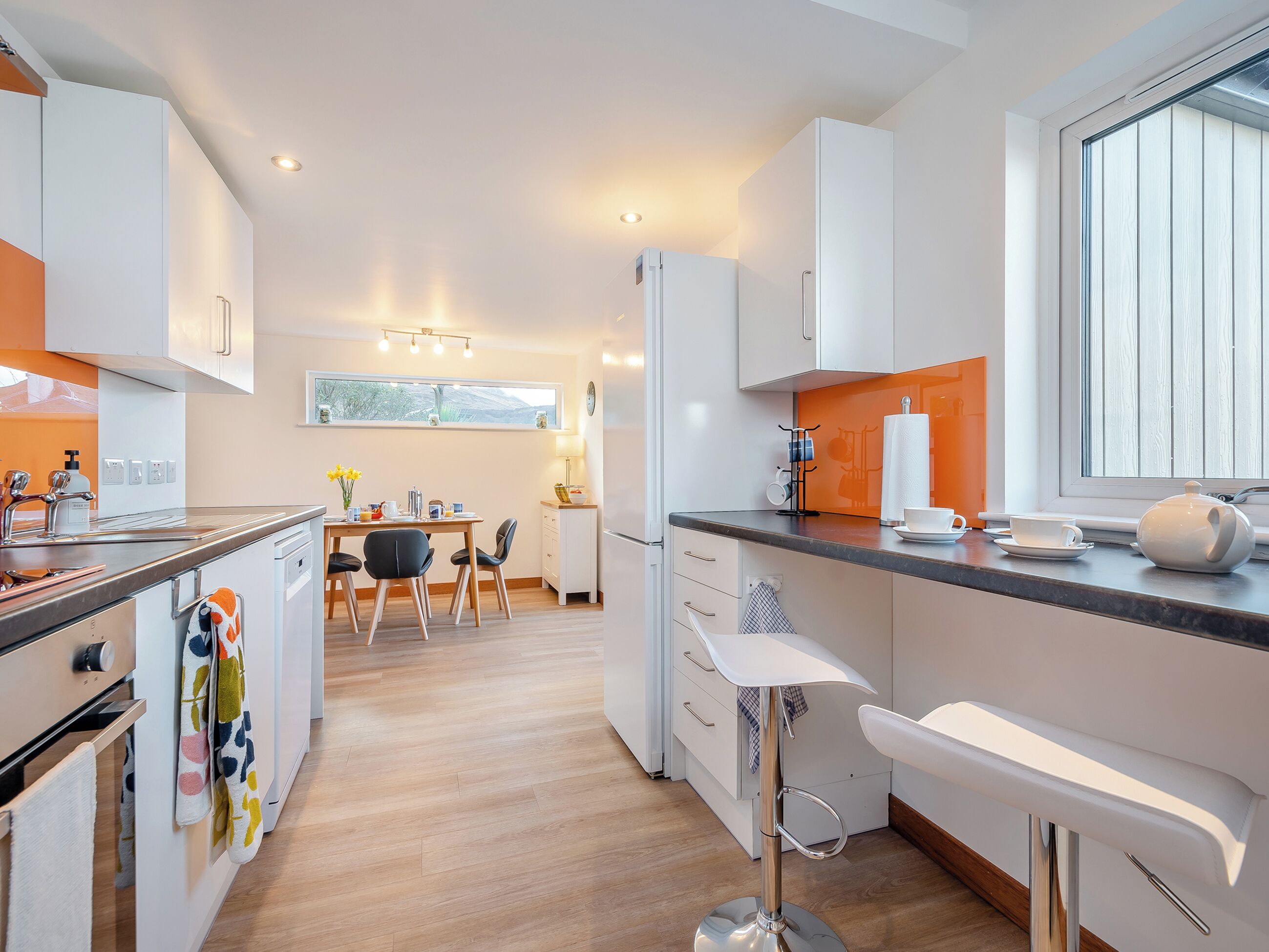 A modern kitchen with white cabinets, a wooden dining table, and a bar stool.