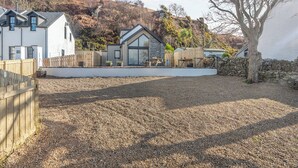 A modern house with a large patio area, a stone wall, and a view of a hillside. - 2 bedroom accommodation in Lochranza (Lochranza)